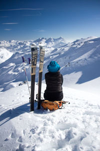 Woman with snowboards sitting on snowcapped mountain against sky