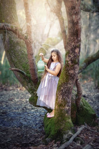 Portrait of woman standing by tree trunk in forest