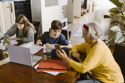 High angle view of senior woman showing smart phone to grandson studying at home