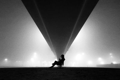 Silhouette person riding motorcycle on sea against sky at night