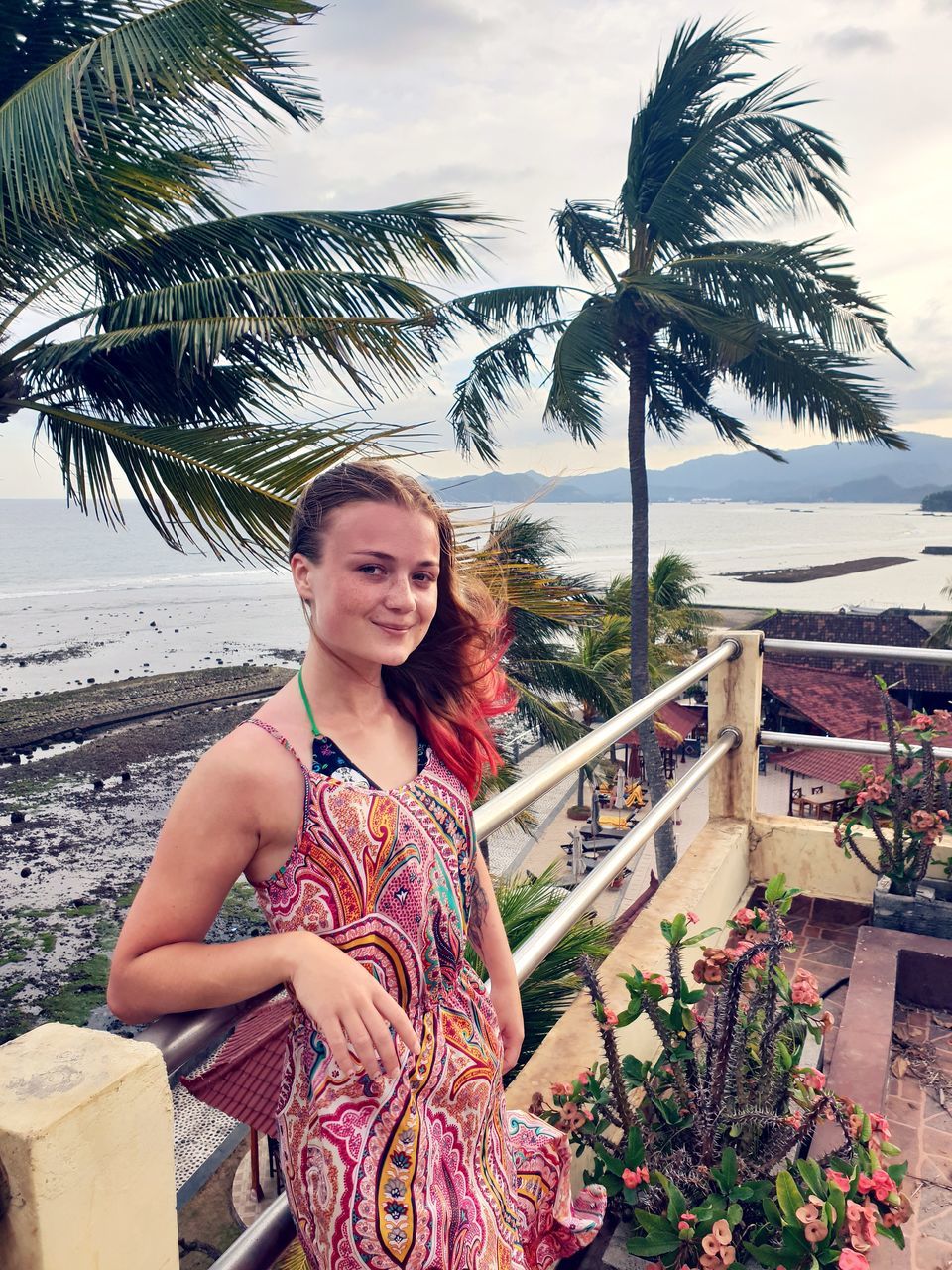 real people, one person, looking at camera, plant, smiling, portrait, young adult, tree, young women, leisure activity, lifestyles, nature, palm tree, tropical climate, standing, happiness, women, architecture, three quarter length, beautiful woman, outdoors, hairstyle