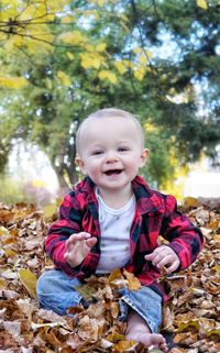 Cute baby boy sitting pile of leaves smiling at camera