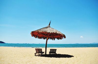 Thatched roof parasol with deck chairs on beach against sky