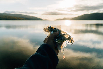 Silhouette of male hand holding plastic trash found on beach at loch ness, scotland.