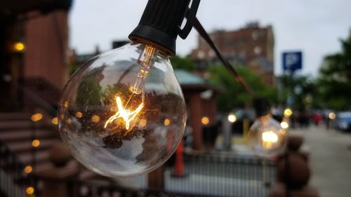 Close-up of illuminated light bulb hanging on street