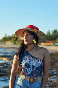 Young woman looking away while standing against hat