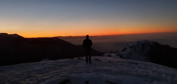 Rear view of silhouette man standing on mountain against sky during sunset