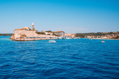 Scenic view of sea by buildings against clear blue sky