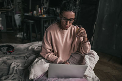 Woman drinking while using laptop at home