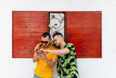 Young couple holding smart phone while standing against wall