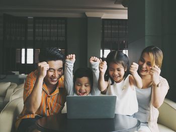Happy family celebrating while looking at laptop on table