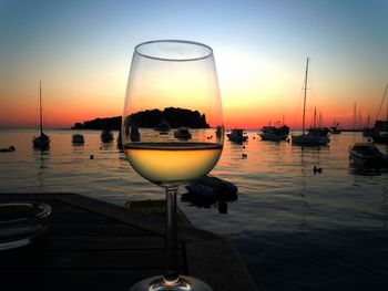 Glass of wine against boats in sea during sunset