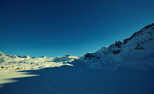 Scenic view of snow covered mountains against clear blue sky