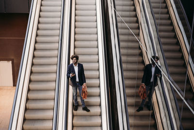 Businessman holding bag moving down from escalator