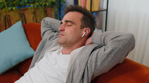 Man with eyes closed listening music through wireless in-ear headphones at home