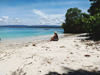 Woman sitting on beach against sky