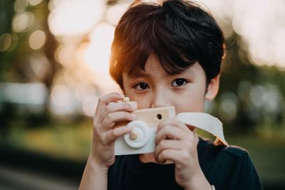 Portrait of boy with toy camera standing at park during sunset