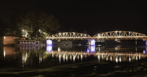 Illuminated bridge over river against sky at night