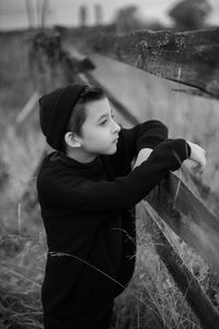 Boy in black clothes stand in a field with an old wooden horse fence in the fall