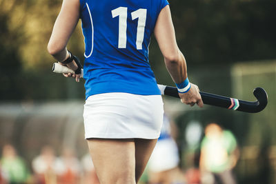 Midsection of hockey player holding bat while walking in stadium