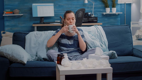 Ill woman drinking tea while sitting on sofa at home
