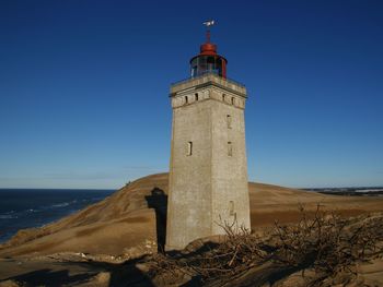 Lighthouse by sea against clear blue sky