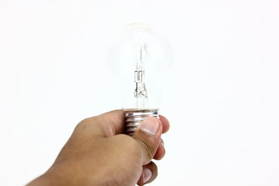 Close-up of hand holding light bulb over white background