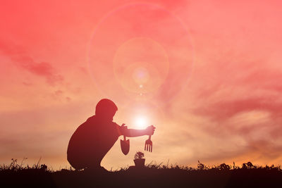 Silhouette boy planting on field against sky during sunset