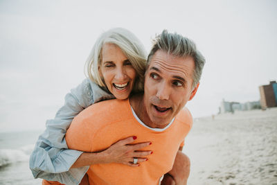 Man giving piggyback ride to happy girlfriend standing at beach