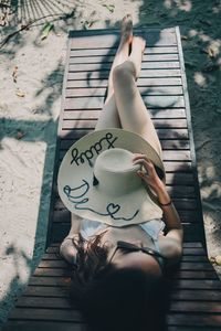 Directly above shot of young woman holding sun hat while relaxing on deck chair at beach