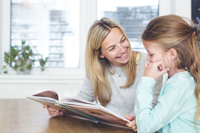 Girl with mother reading book at home