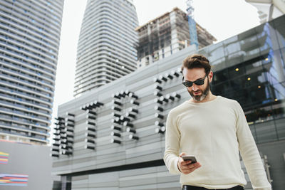 Low angle view of young man standing by building in city