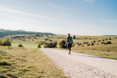 Rear view of man walking on field against sky