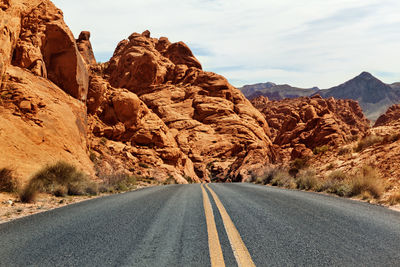 Diminishing perspective of road leading towards mountains against sky during sunny day