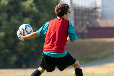 Rear view of boy playing soccer goalkeeper preparing to throw soccer ball