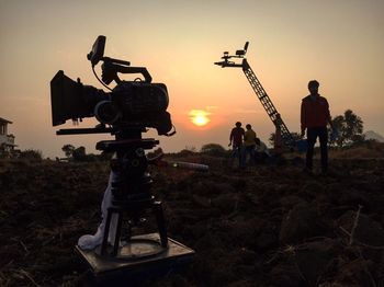 Silhouette photographing on field against sky during sunset