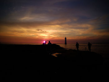 Silhouette people on beach against sky during sunset