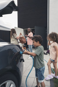 Boy charging electric car with family at front yard
