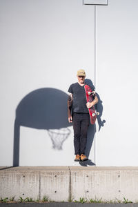 Portrait of adult male jumping holding skateboard in bright sunlight