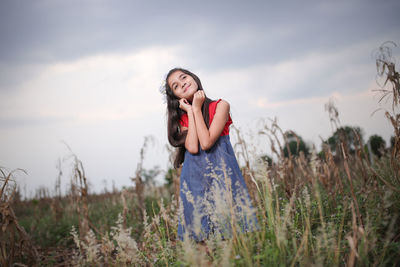 Smiling cute girl standing amidst plants on field during sunset