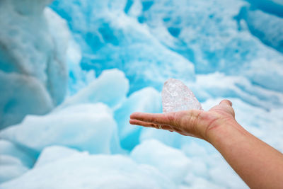 Cropped image of person hand holding ice against icebergs