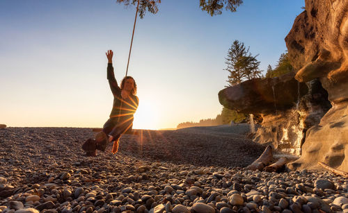 Man standing on rock at beach against sky during sunset