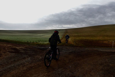 Rear view of man riding bicycle on field