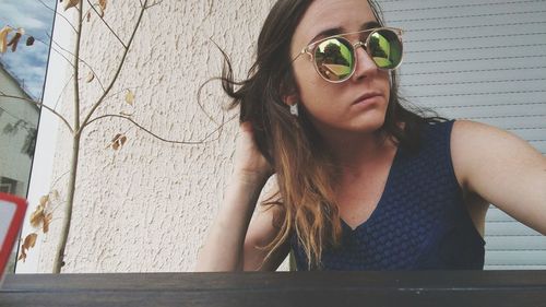 Close-up of young woman wearing sunglasses against wall