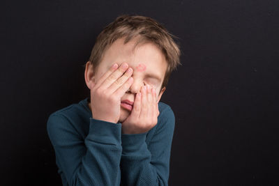 Close-up of man covering face against black background