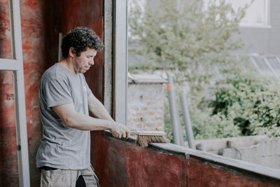 Caucasian male builder sweeps a window frame with a broom.