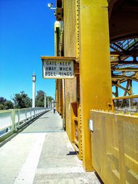 Sign board over walkway of bridge against sky