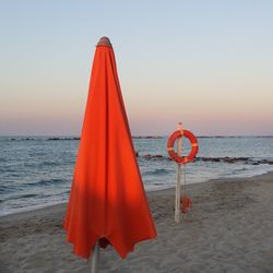 Red flag on beach against clear sky during sunset