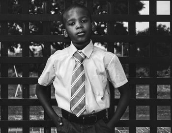 Portrait of boy in school uniform standing against fence