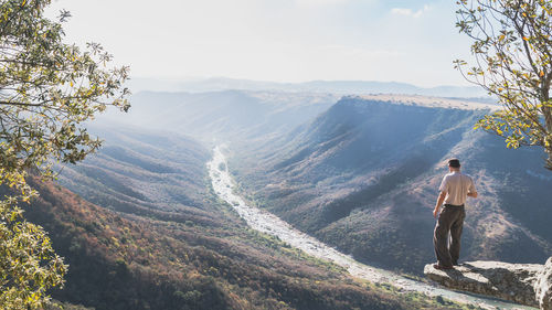 Man standing on cliff while looking at mountains against sky